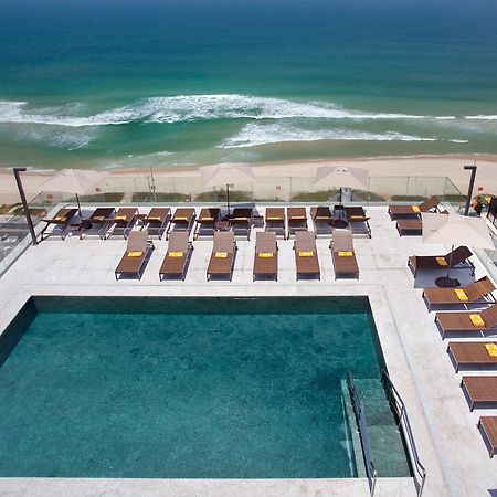 Hotel Windsor Marapendi Rio de Janeiro Exterior foto The photo shows a rooftop area with a swimming pool and several lounge chairs arranged around it. The pool has a clear blue surface, and the lounge chairs are positioned in a neat row, some with yellow cushions. In the background, you can see a beaut